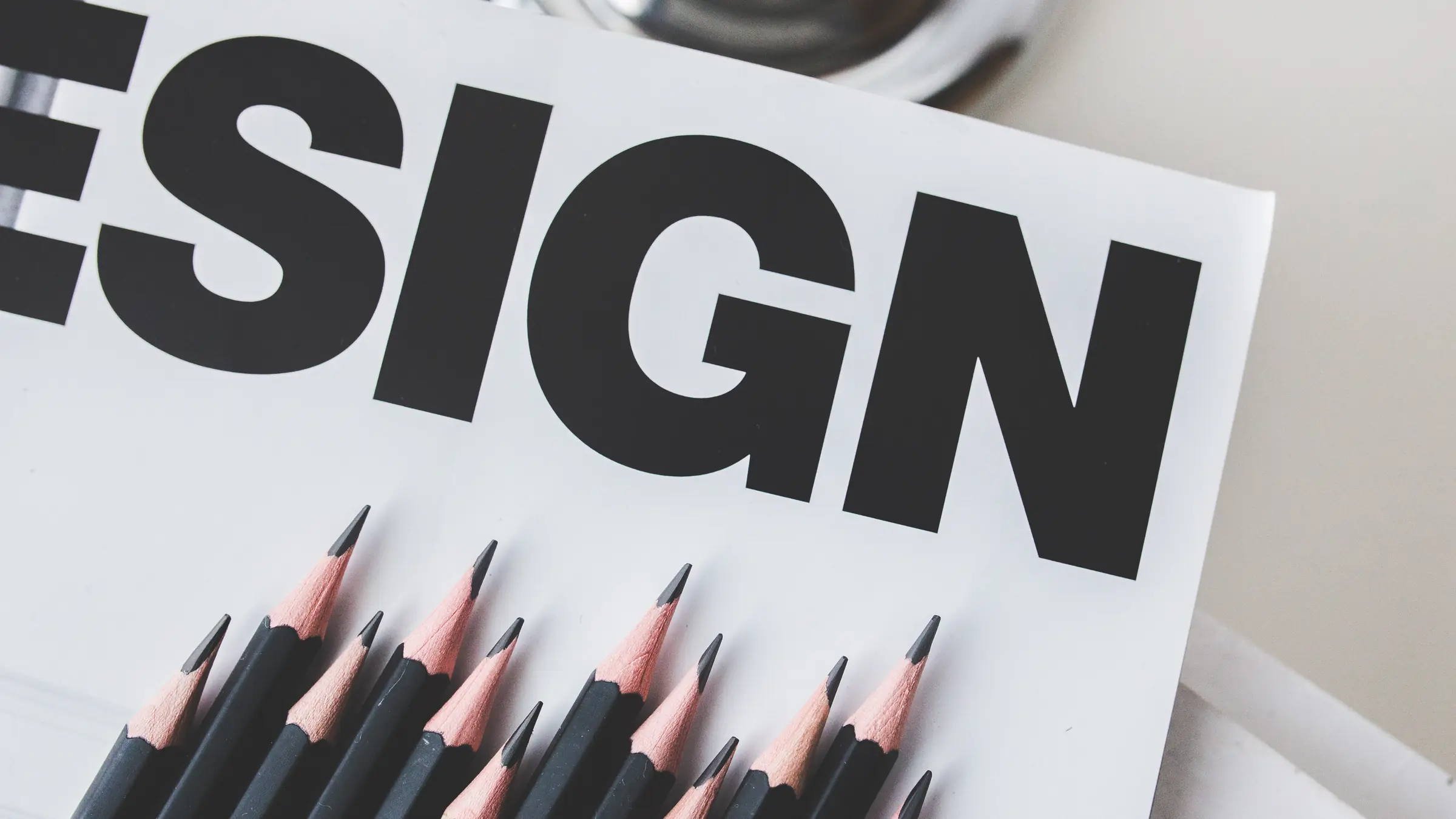 Gespitzte schwarze Bleistifte vor dem großen Schriftzug „Design“ auf weißem Papier