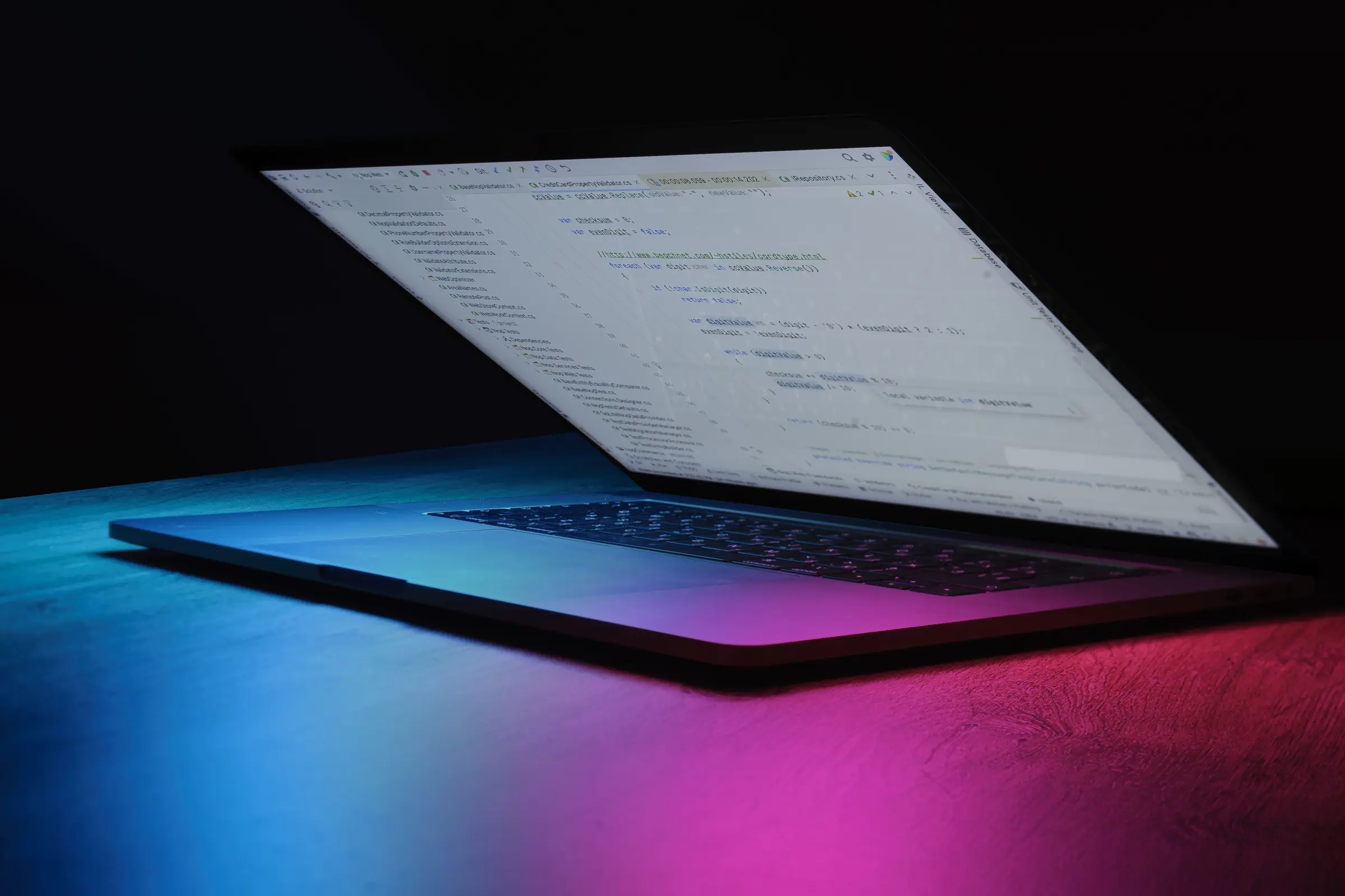 Aufgeklappter Laptop mit Quellcode im Dunkeln, von blauem und pinkem Licht angestrahlt